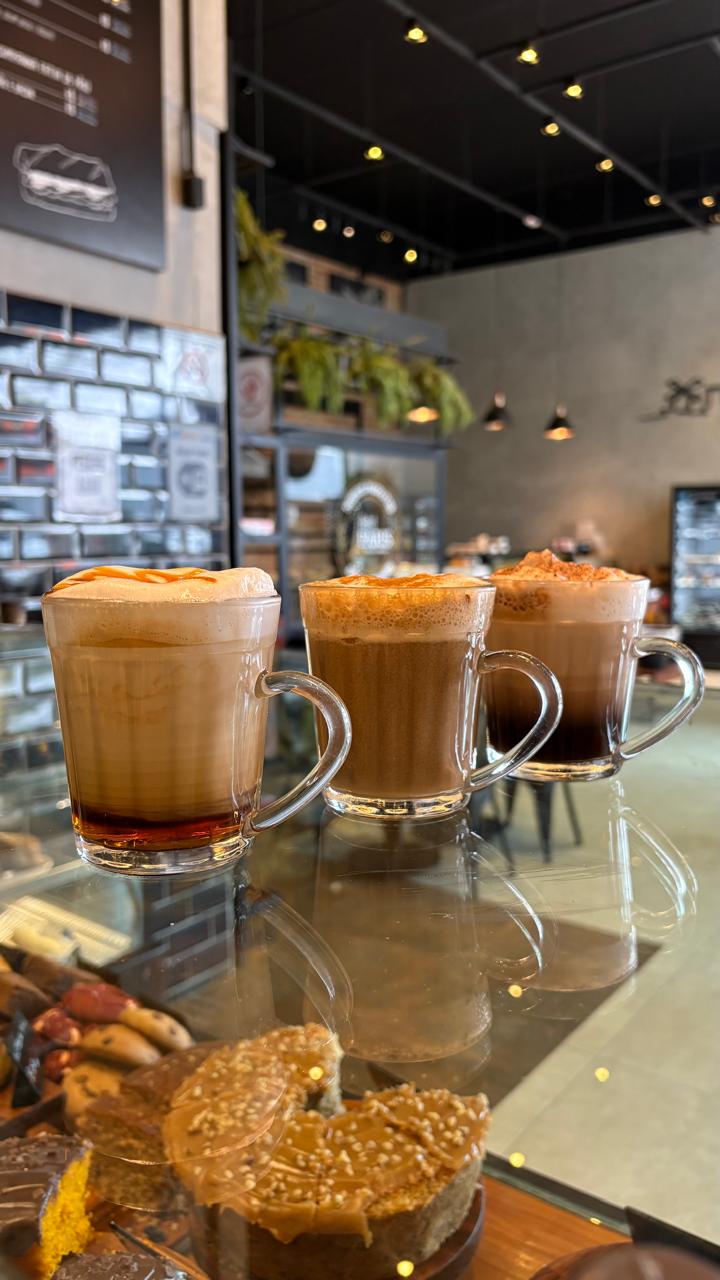 Interior de cafeteria Cafelli, balcão de mármore com máquina de espresso ao lado de plantas e janela com luz quente